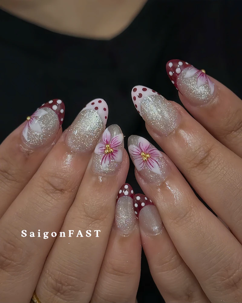 Burgundy and white polka-dot nail tips with silver glitter and pink flowers